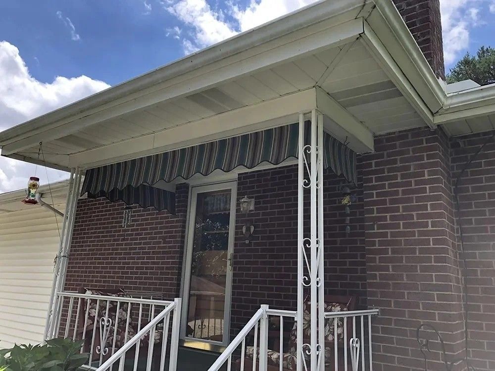 Brick house with porch, awning, and decorative white railings. The front door is visible.
