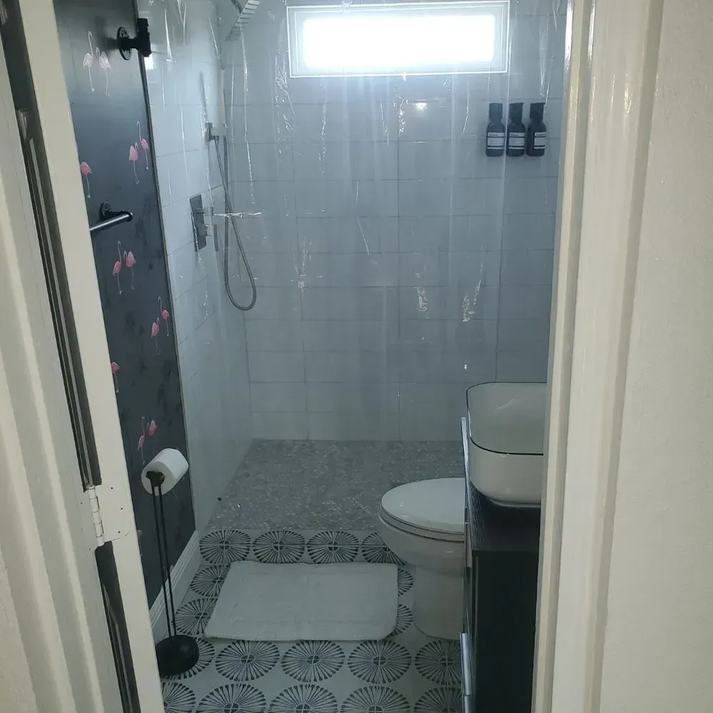 Small bathroom with shower, toilet, and sink. Features patterned floor, flamingo wallpaper, and a shower curtain.