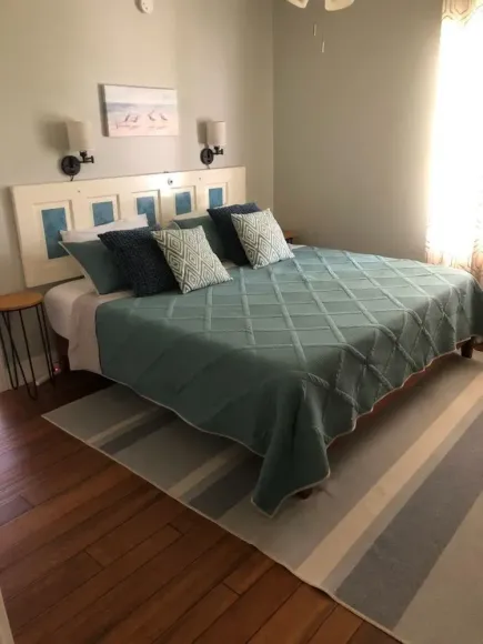 Bedroom with repurposed door headboard, blue quilt, pillows, wooden floor, and striped rug.