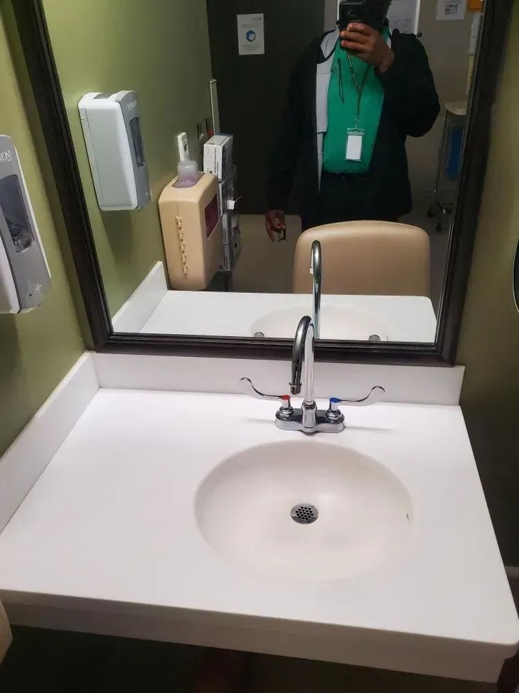 Person in a green scarf in a public restroom with a white sink and mirror.