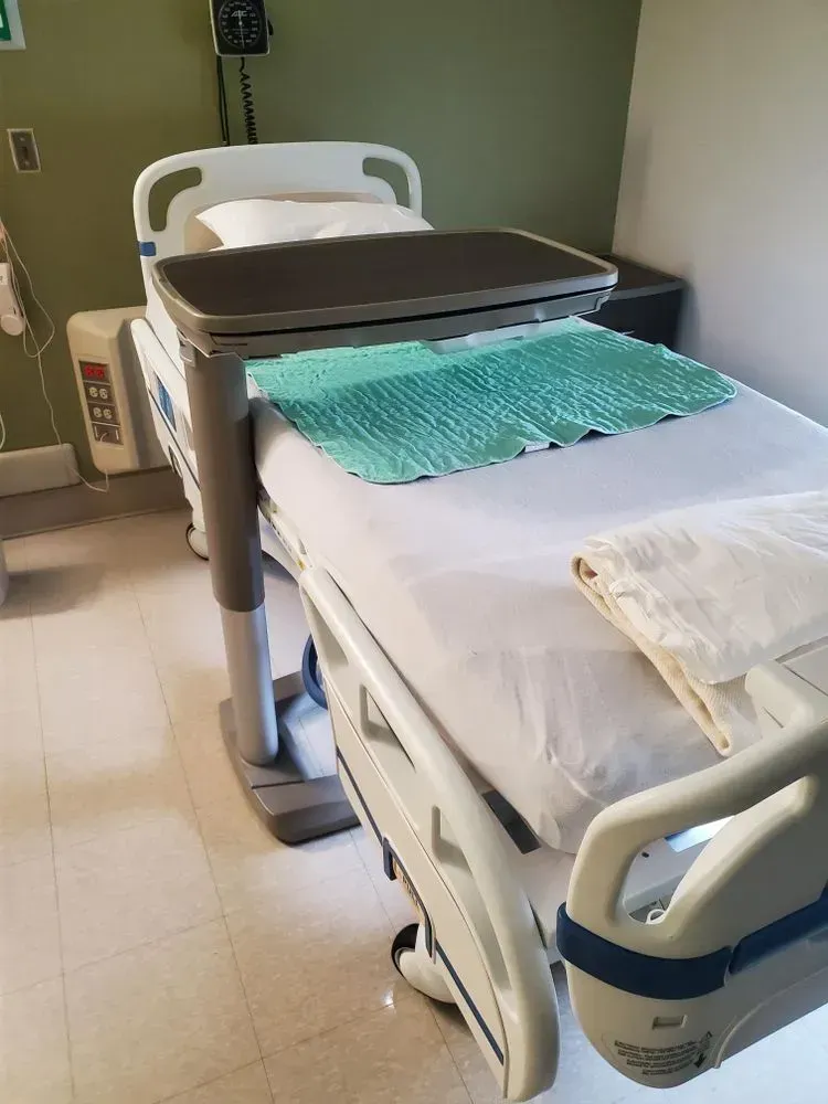 Hospital bed with adjustable tray and teal mat.
