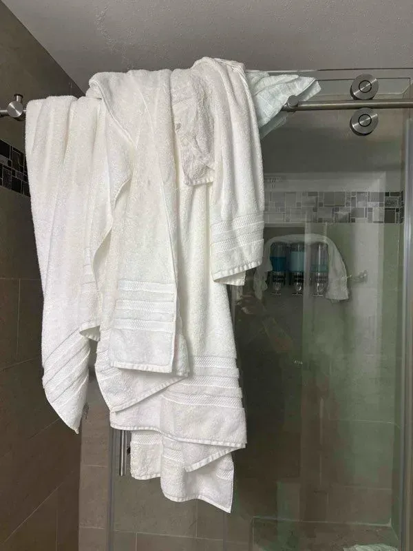 White towels draped over a shower rod inside a glass shower stall.