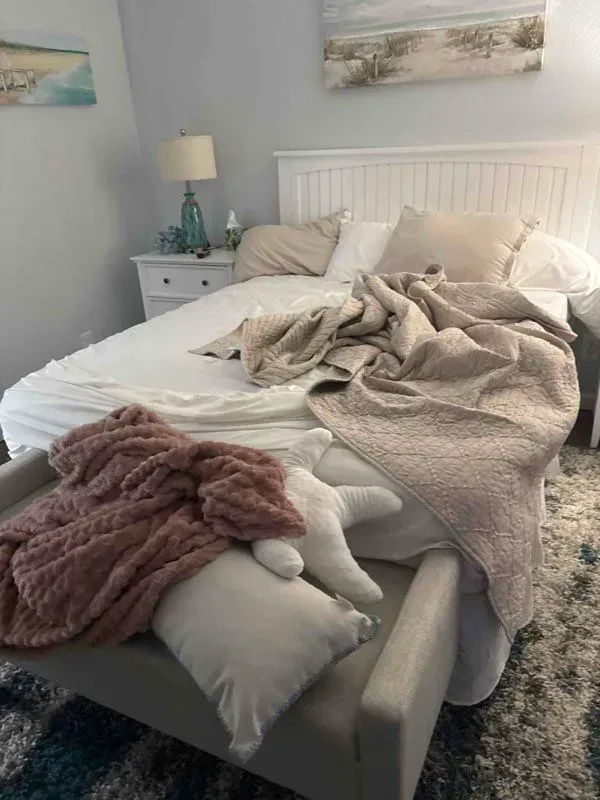 A messy white bed with a dog ramp. Blush-colored blankets and pillows, a nightstand with a lamp.