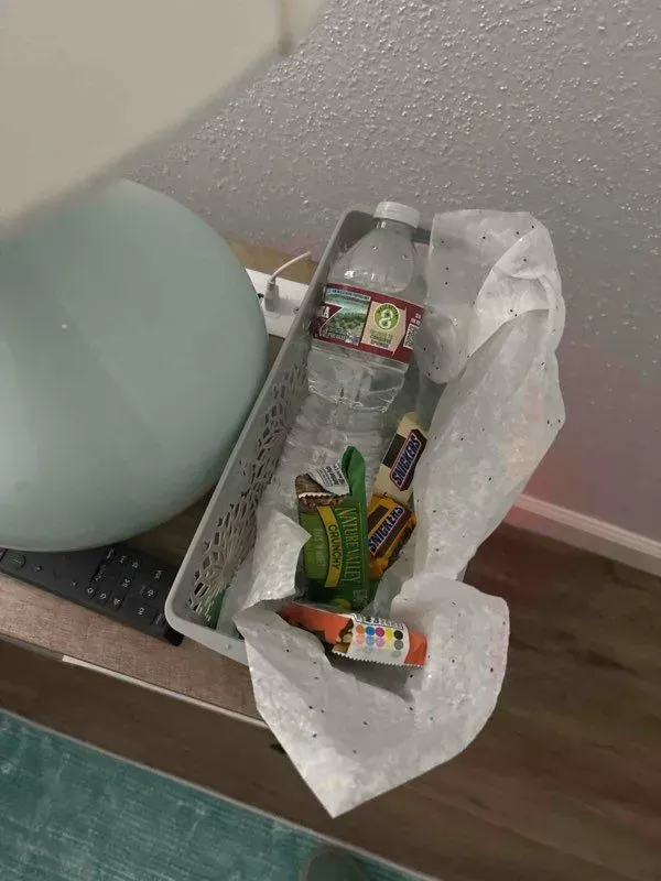 A water bottle and snacks sit in a basket on a table next to a blue ball.