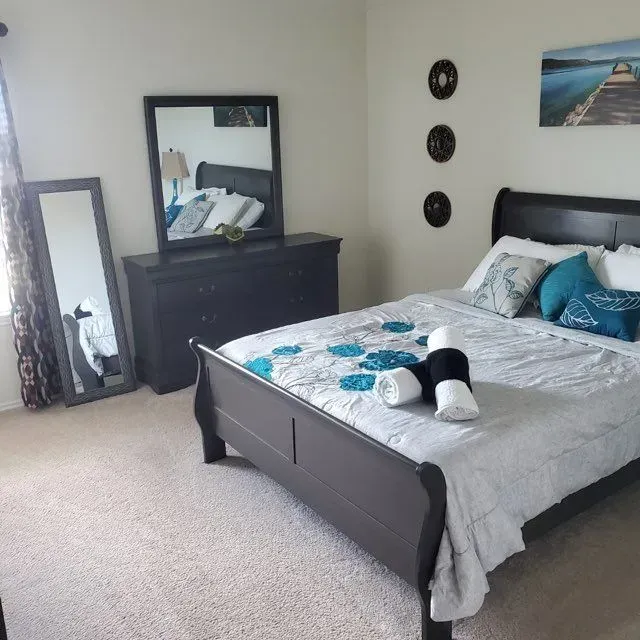 Bedroom with dark furniture, bed with blue accents, full-length mirror, dresser, and wall art.