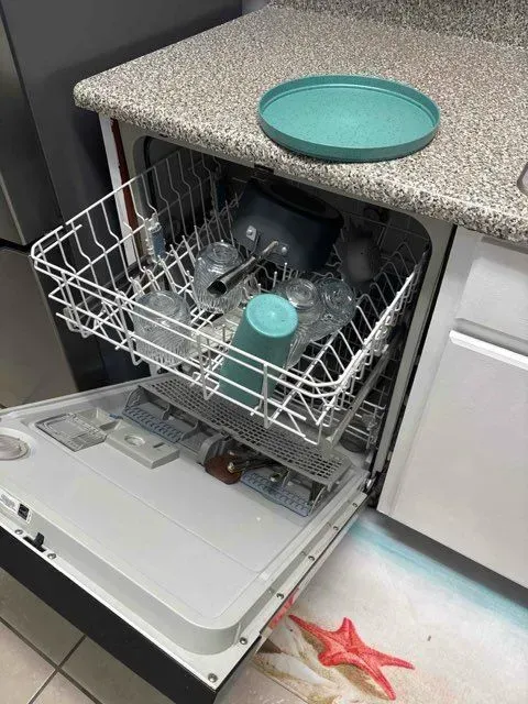 Dishwasher open, filled with dishes; turquoise plate on countertop.