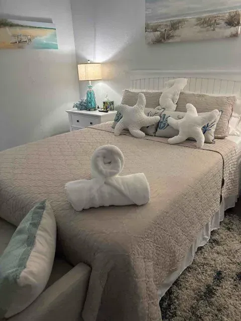 Bedroom with a beige bed, starfish pillows, and a towel swan; beach-themed decor.
