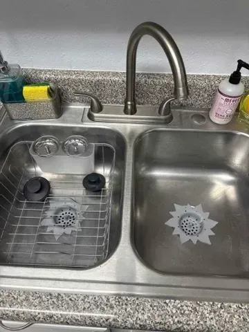 Stainless steel kitchen sink with faucet, dish soap, and sponge holder. Sink has two basins, one with a dish rack.
