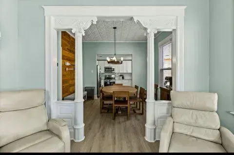 Two beige recliners face an ornate white doorway into a dining area with a wooden table.