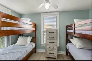 Two bunk beds in a room with light blue walls, a window, and a white dresser.