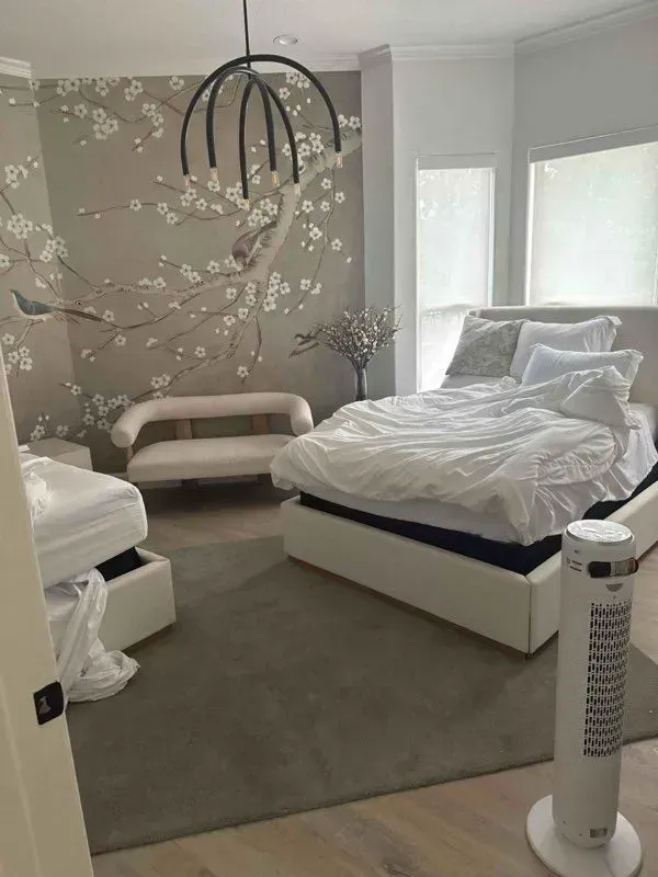 Bedroom with floral wallpaper, bed, sofa, and a fan. Soft colors; a modern aesthetic.