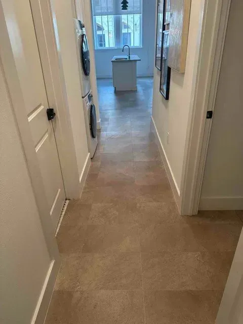 Hallway with beige flooring, white walls, and a view into a kitchen with an island.
