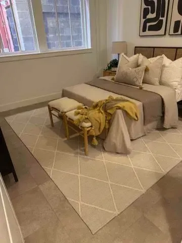 Bedroom with bed, bench, and cream-colored rug. Neutral tones, soft lighting, and modern artwork.