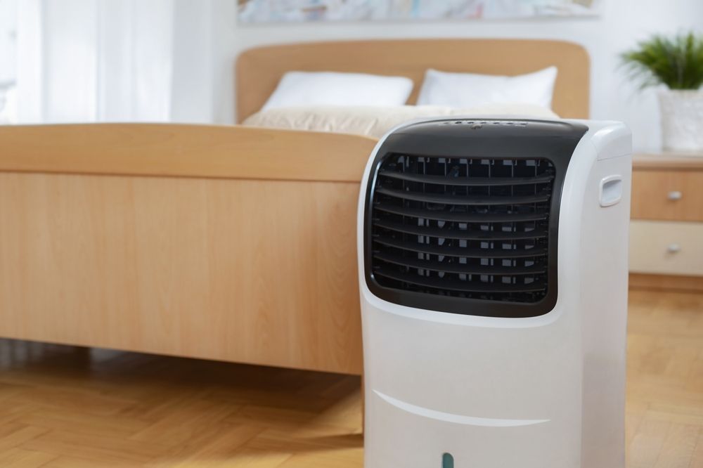 A portable air conditioner is sitting next to a bed in a bedroom.