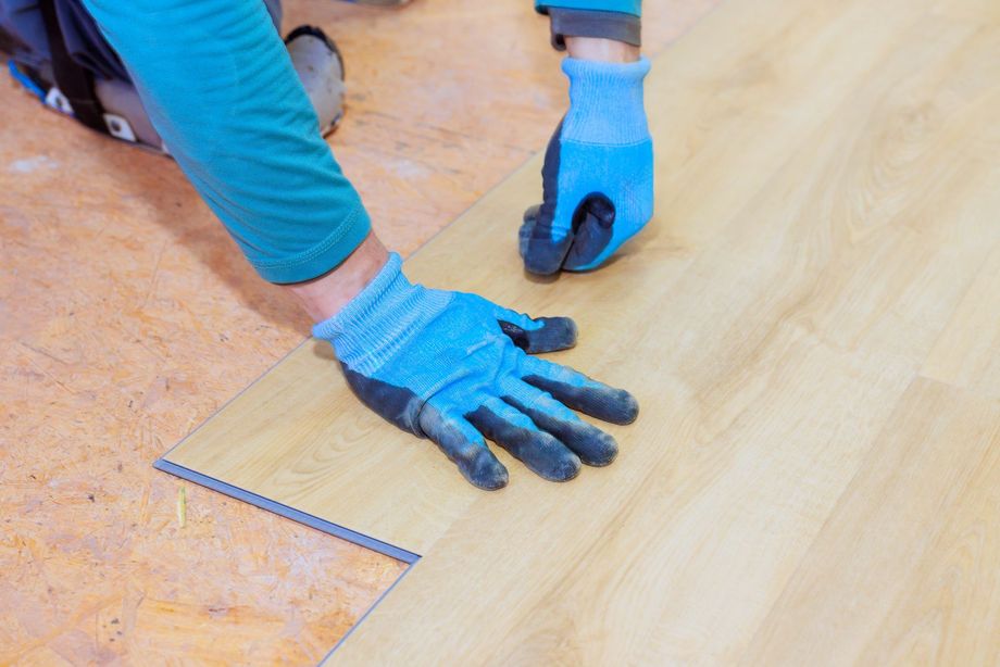 Una persona posa delle piastrelle bianche sul pavimento, usando un martello per fissarle.