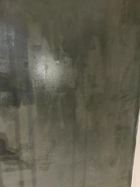 Parete dipinta di grigio con pennellate visibili e una macchia più chiara e luminosa.