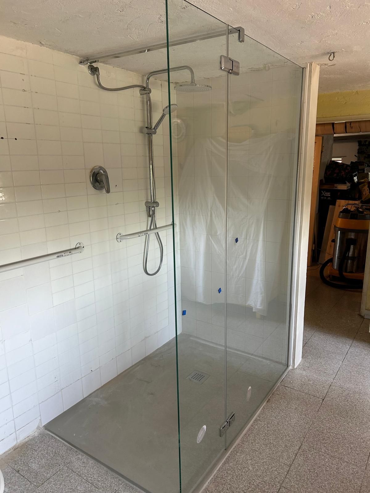 Box doccia in vetro con base grigia, accessori cromati e pareti piastrellate bianche.