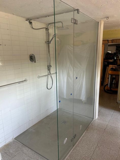 Box doccia in vetro con base grigia, accessori cromati e pareti piastrellate bianche.