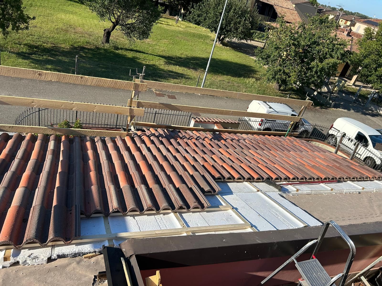 Tetto in costruzione con tegole rosse e ringhiera di sicurezza; un furgone bianco è parcheggiato nelle vicinanze.