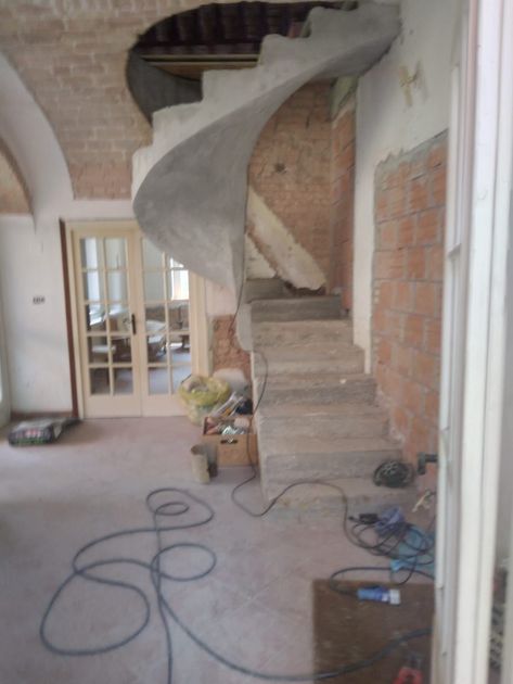 Scala a chiocciola in cemento in costruzione in una stanza con pareti in mattoni a vista.