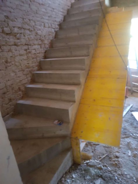 Scala in cemento in costruzione; assi di supporto gialle. Muro di mattoni sulla sinistra.