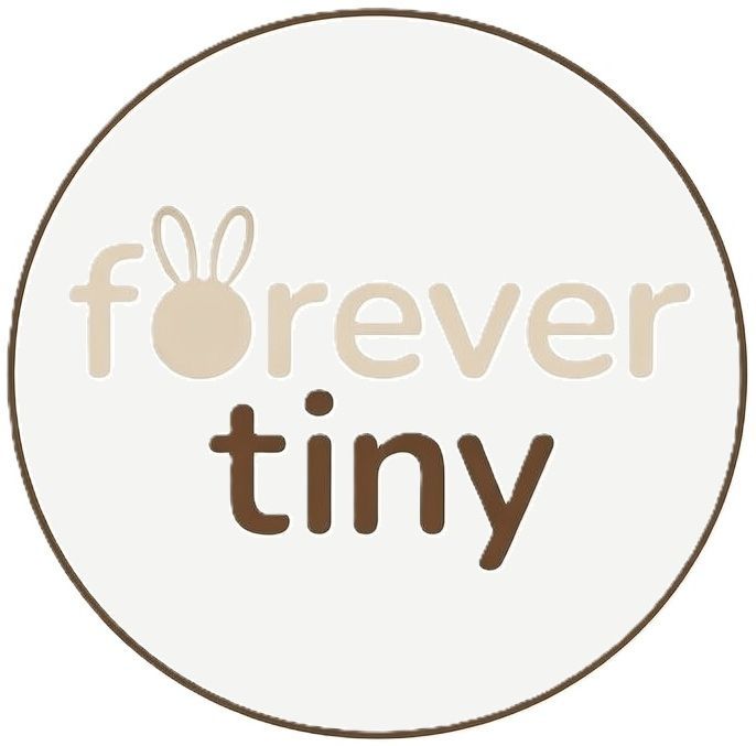 Een rond logo met een beige achtergrond en rand, met de tekst "forever tiny" en konijnenoortjes op de eerste "o".