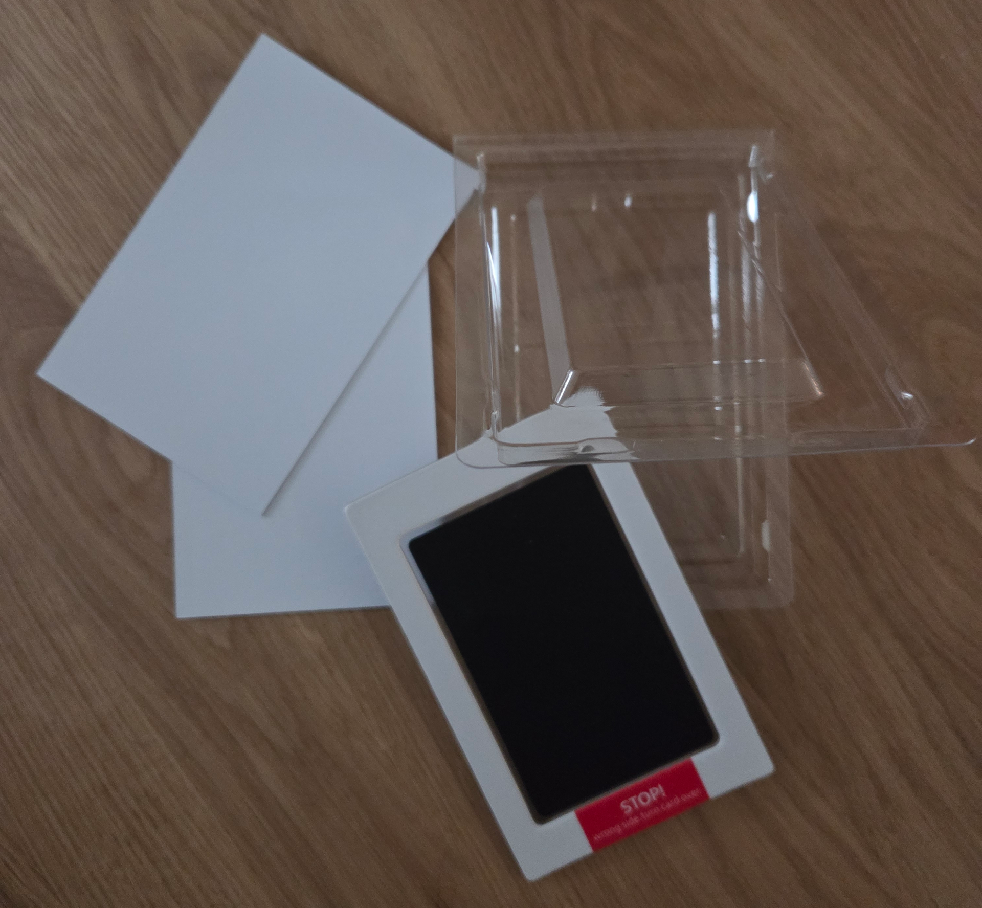 Een stempelkussenset met babyvoetafdrukjes, inclusief een vierkantje zwarte inkt, twee witte vellen karton en een doorzichtige plastic verpakking.