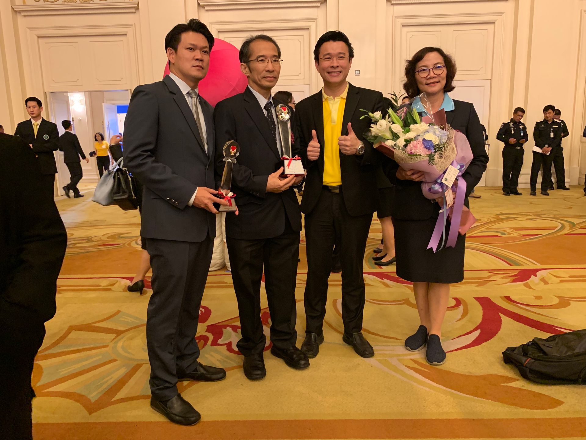 A group of people are standing next to each other in a room holding trophies and flowers.