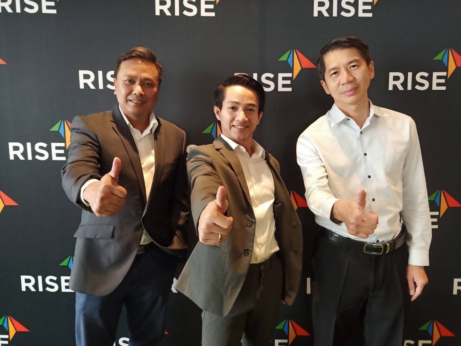 Three men are standing in front of a wall that says rise
