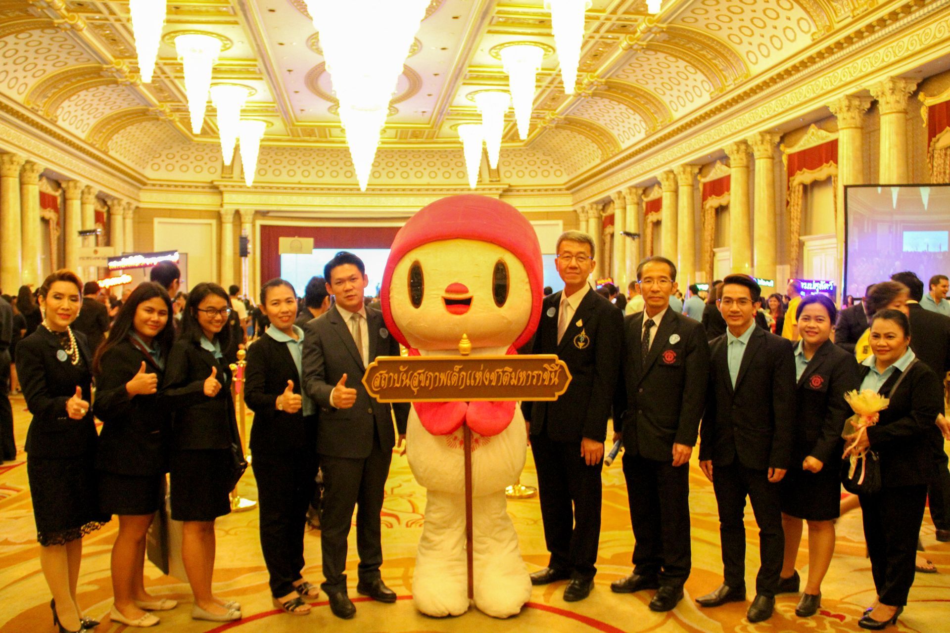 A group of people are posing with a mascot in a large room.