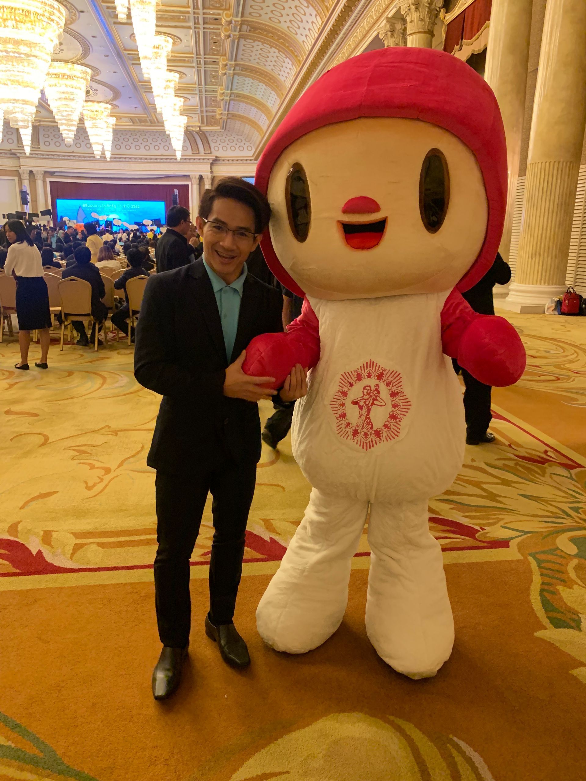 A man in a suit is standing next to a mascot in a room.