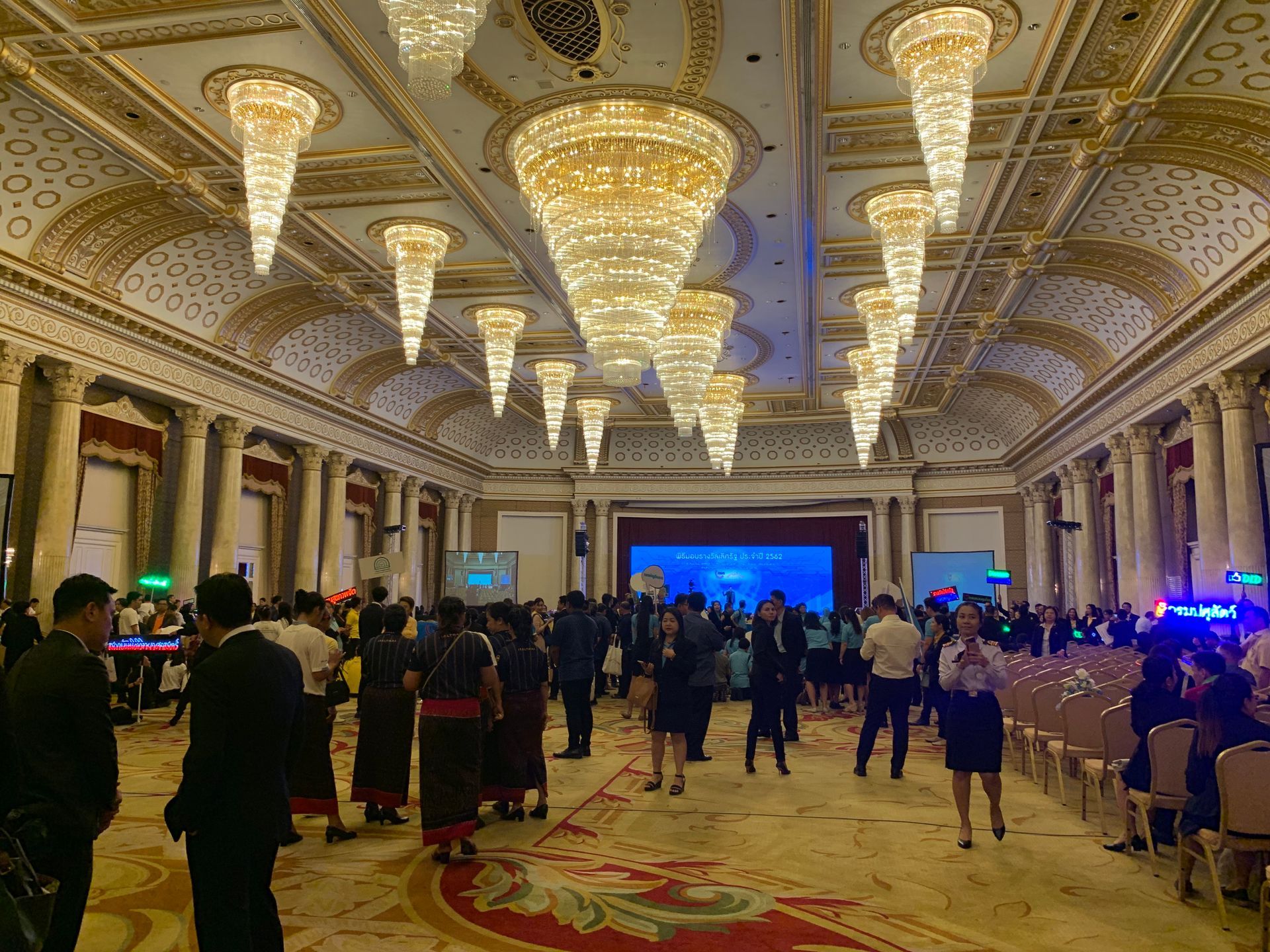 A group of people are standing in a large room with a lot of lights hanging from the ceiling.