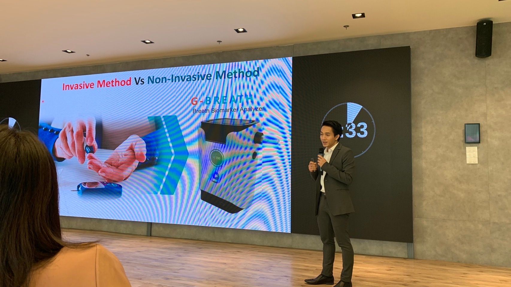 A man in a suit is giving a presentation in front of a large screen.