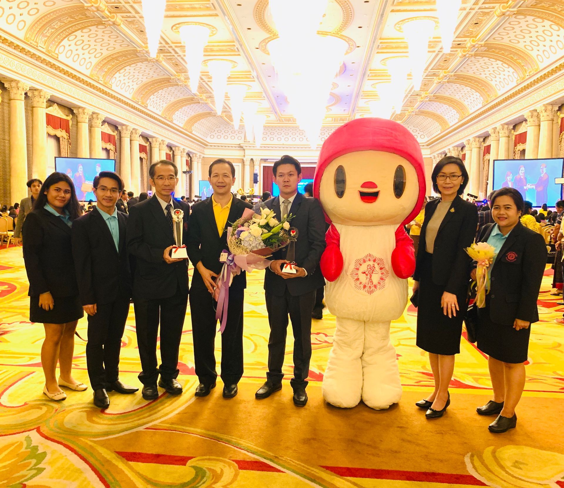 A group of people standing next to a mascot in a large room.