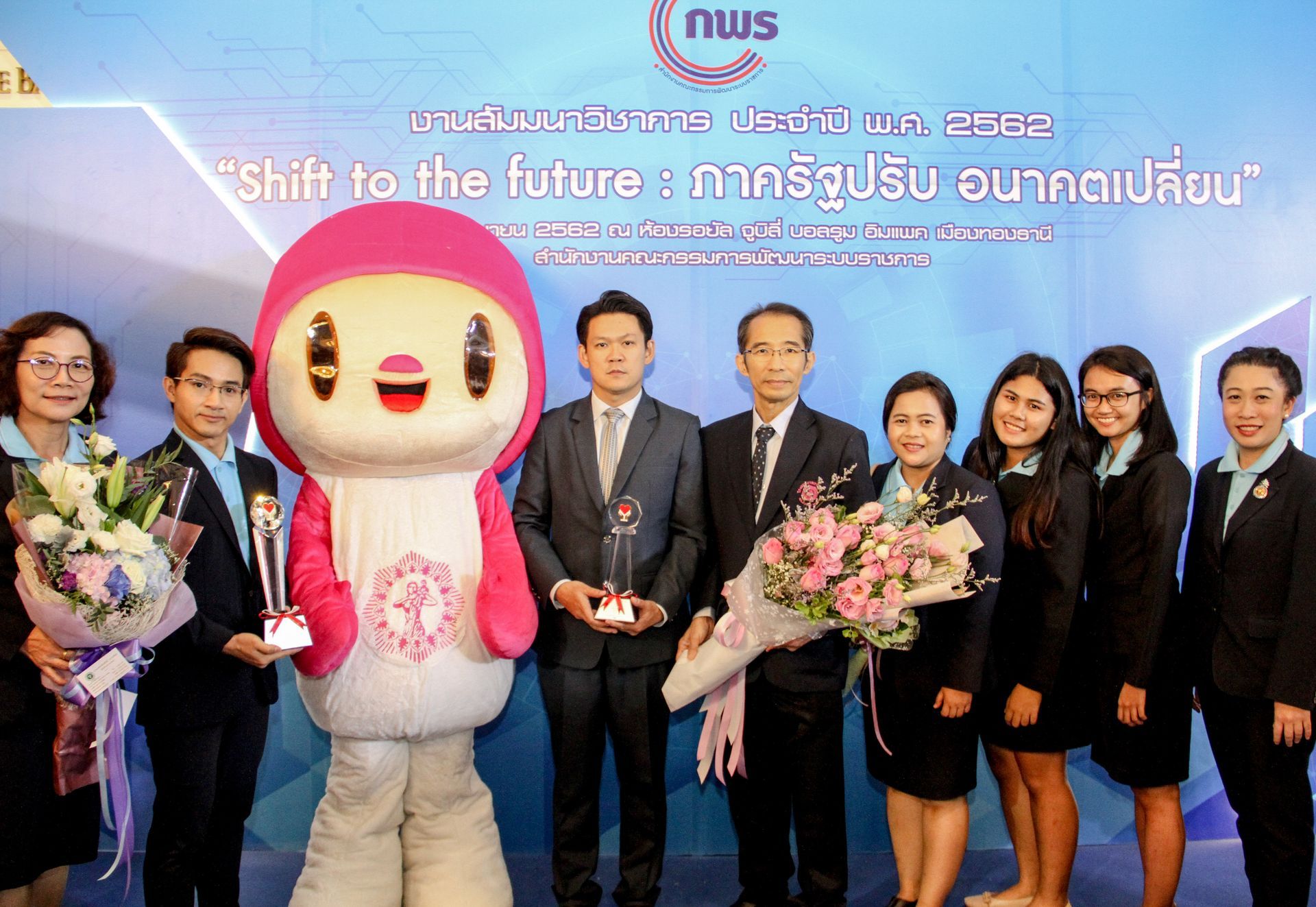 A group of people standing next to a mascot holding flowers.