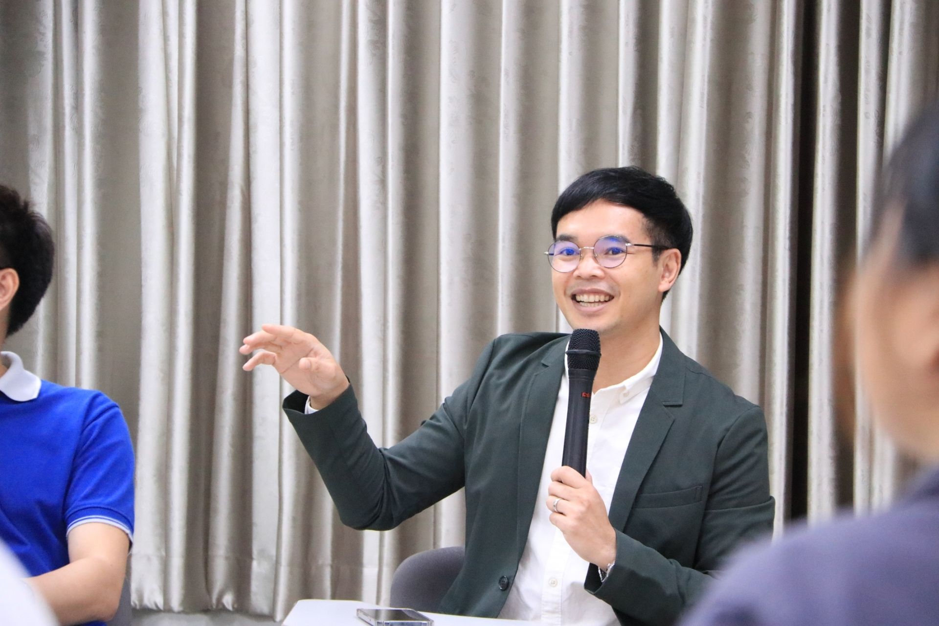 A man in a suit is holding a microphone and talking to a group of people.