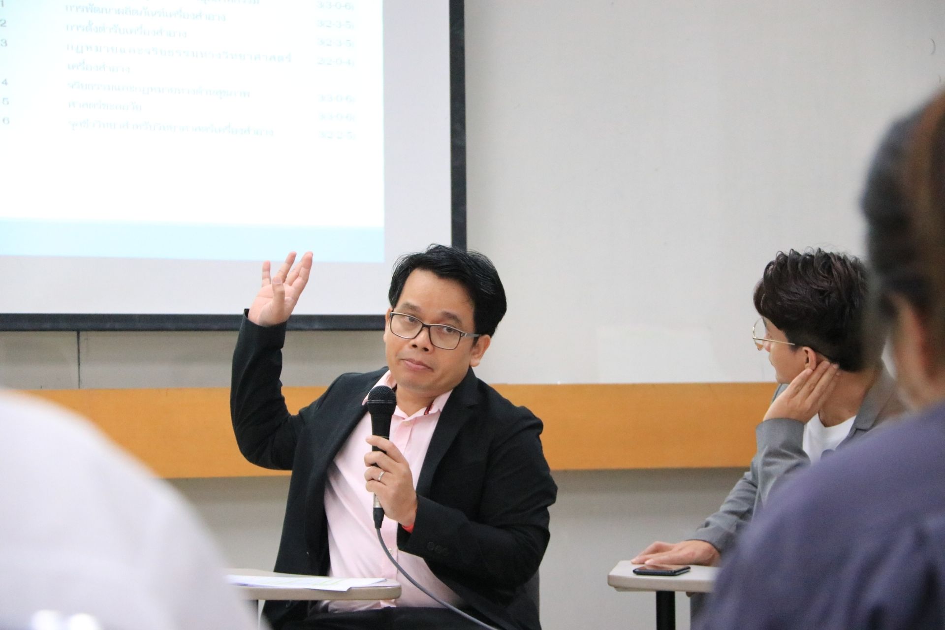 A man is giving a presentation in a classroom while holding a microphone.