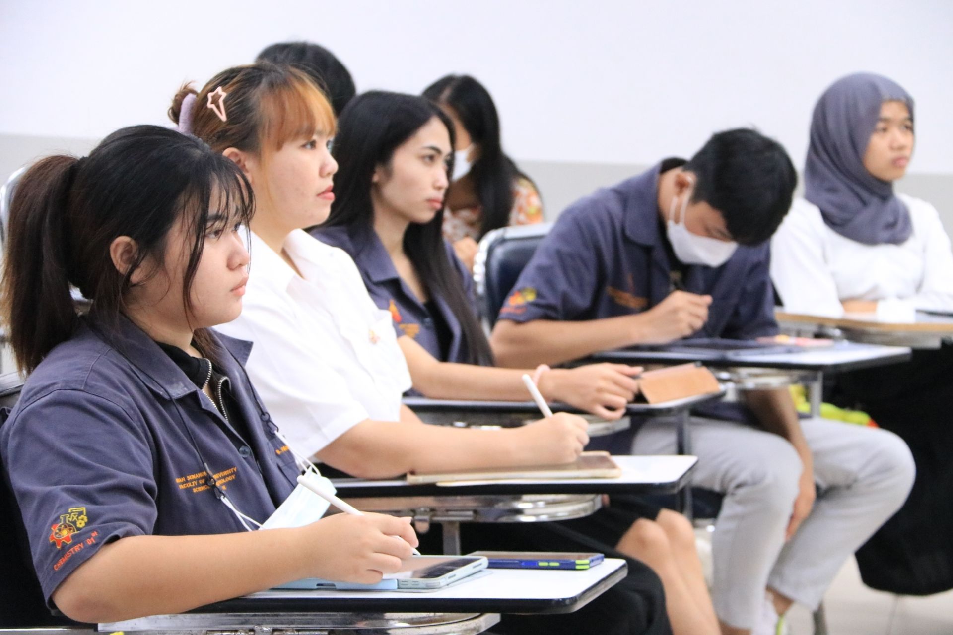 A group of people are sitting at desks in a classroom.