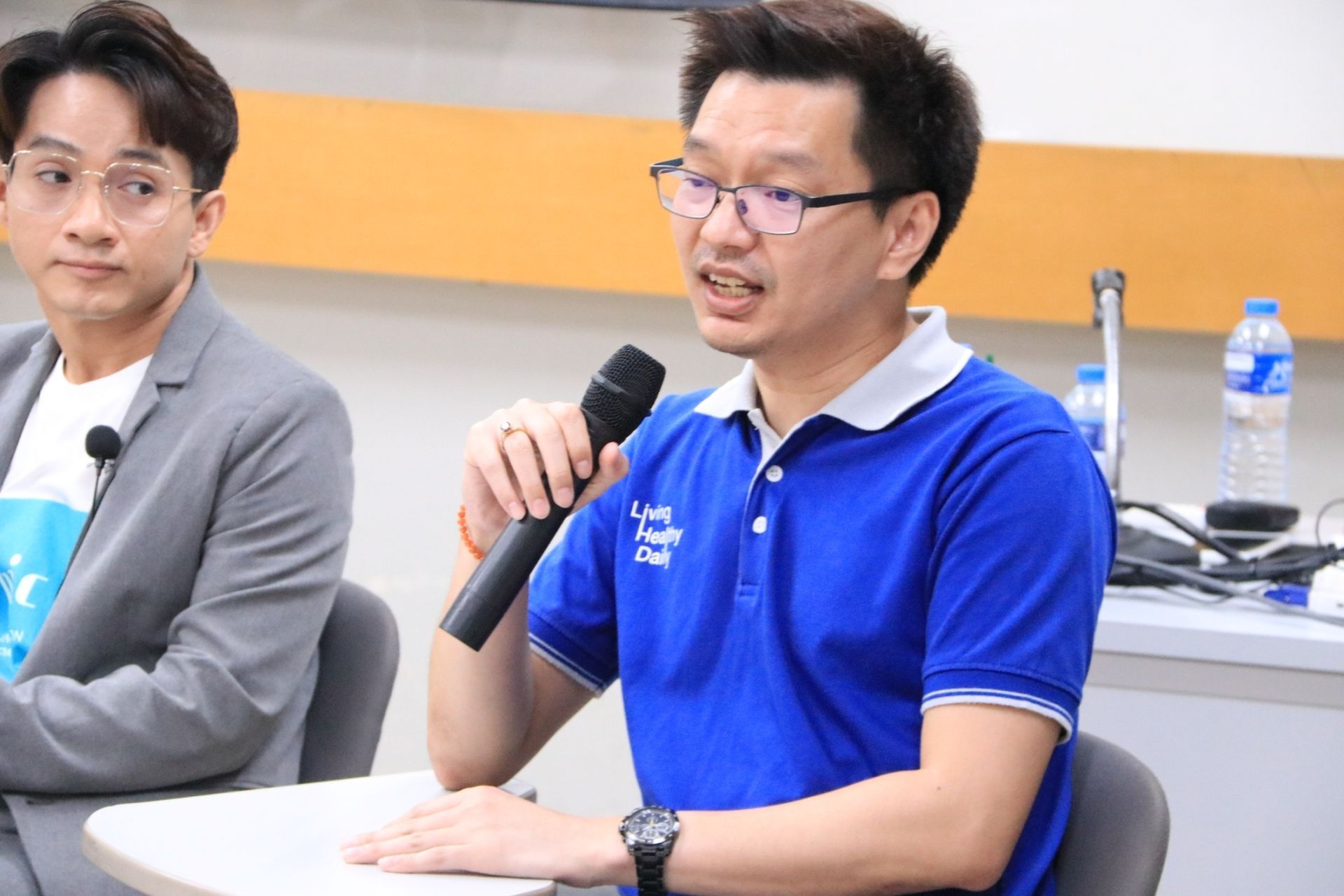 A man in a blue shirt is holding a microphone while sitting at a table.