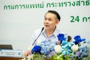 A man is sitting at a table with flowers and a microphone.