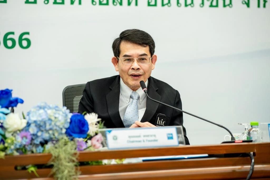A man in a suit and tie is sitting at a table talking into a microphone.