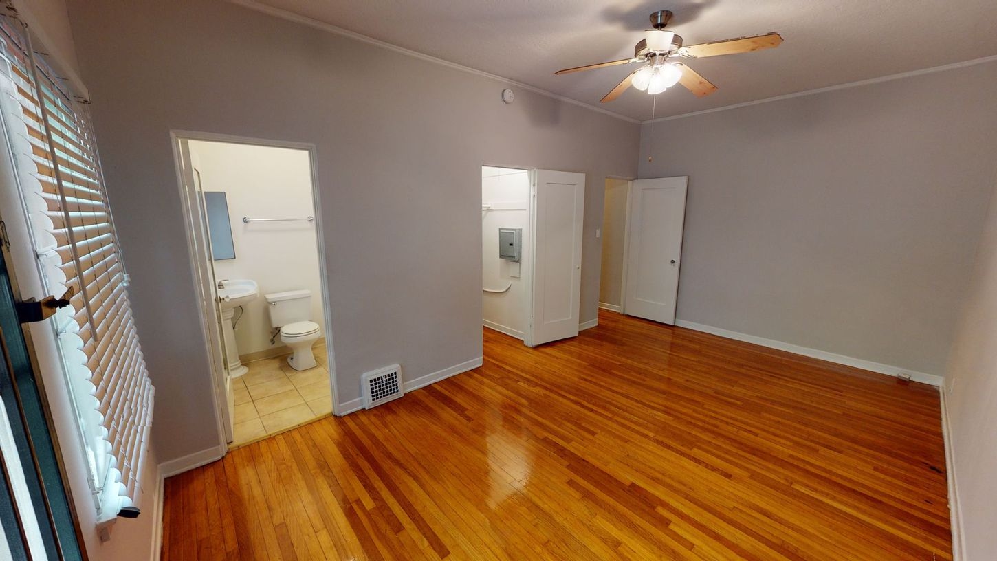 Empty room with hardwood floors, a bathroom, and a ceiling fan.