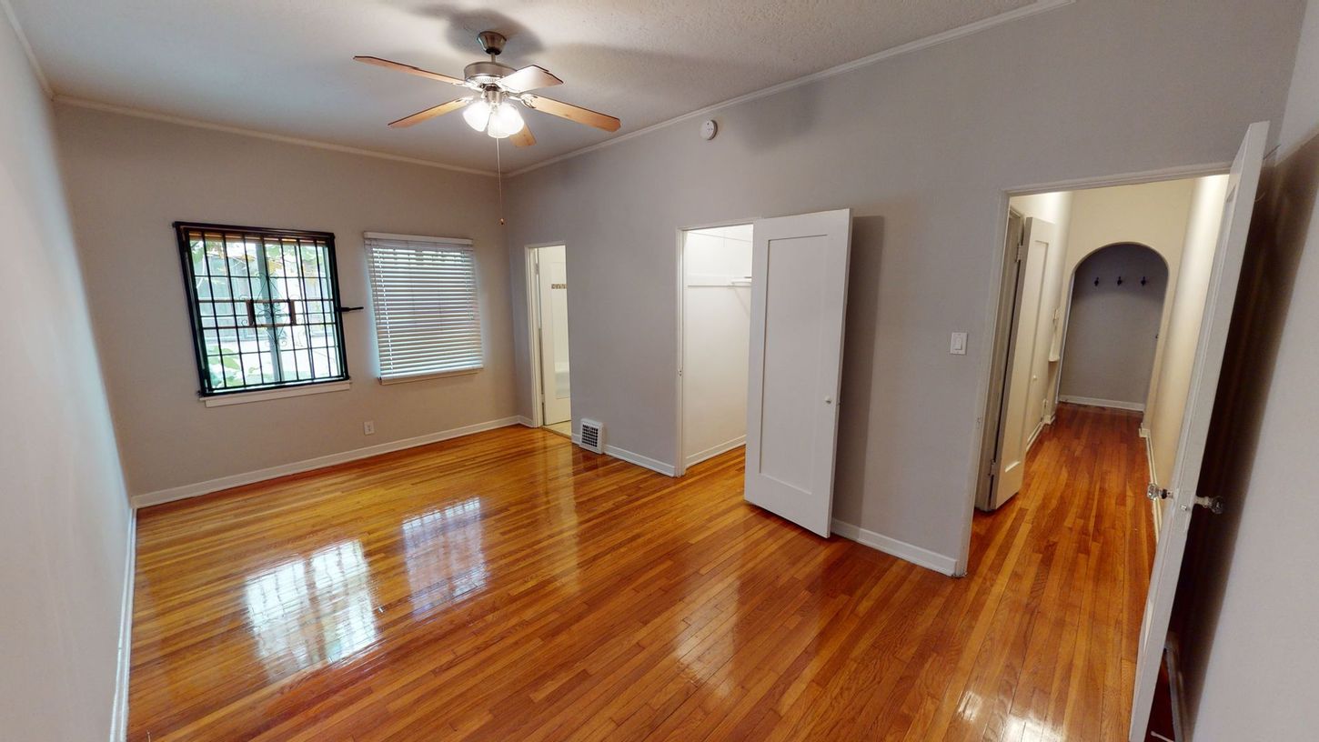 Wooden-floored room with two windows, closet, and doorways leading to other rooms.