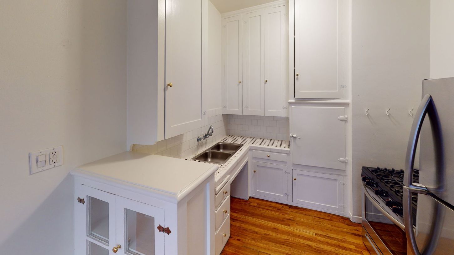 Small white kitchen with cabinets, sink, and gas stove.