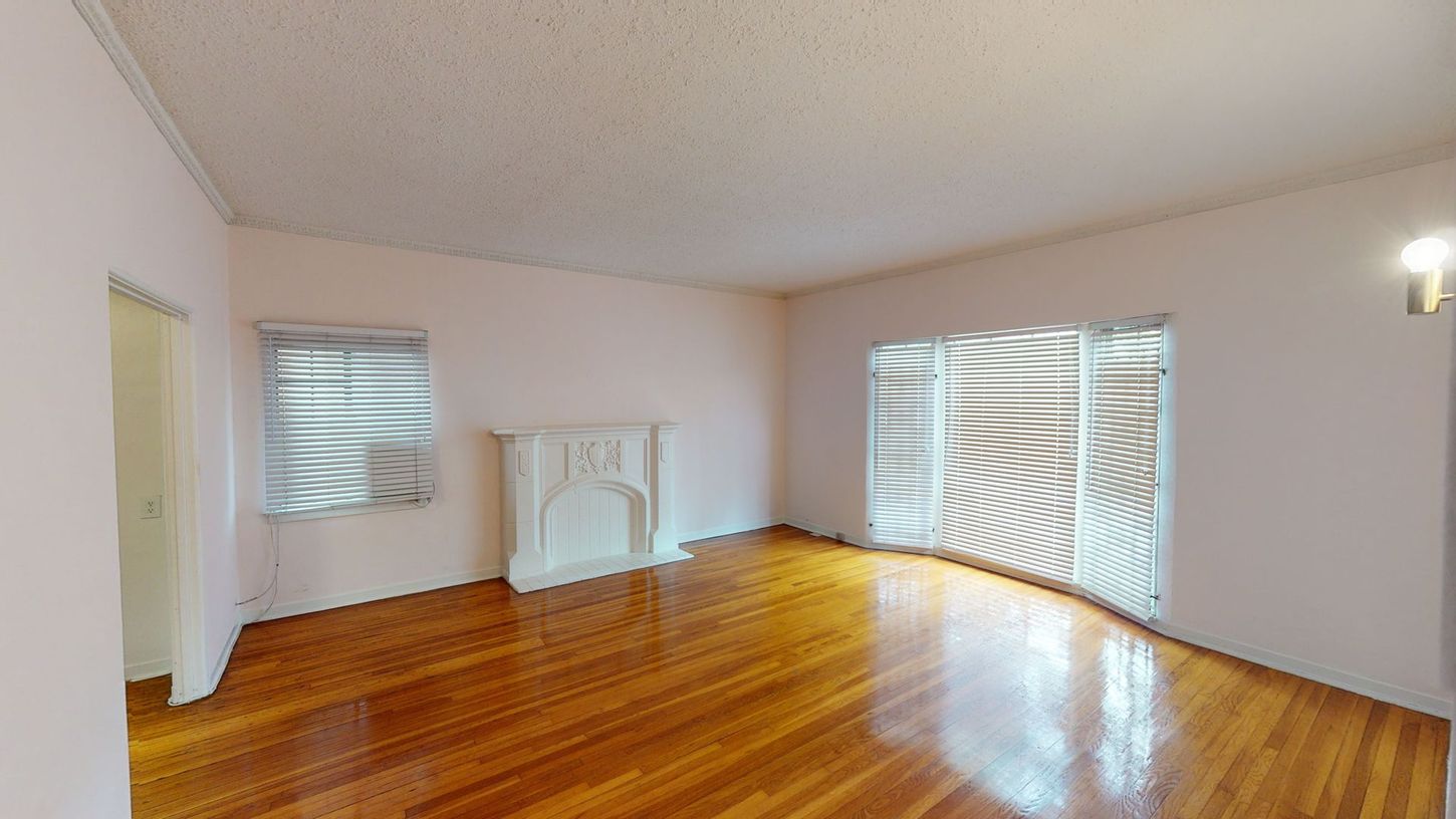 Empty room with hardwood floors, a fireplace, window, and large sliding doors. Pink walls and a white ceiling.