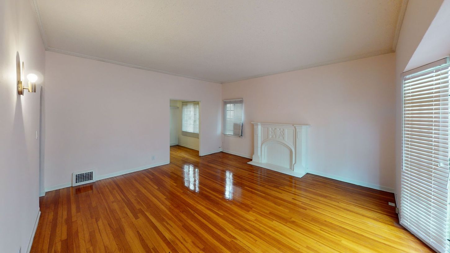 Empty room with wood floors, light pink walls, fireplace, and window with blinds.