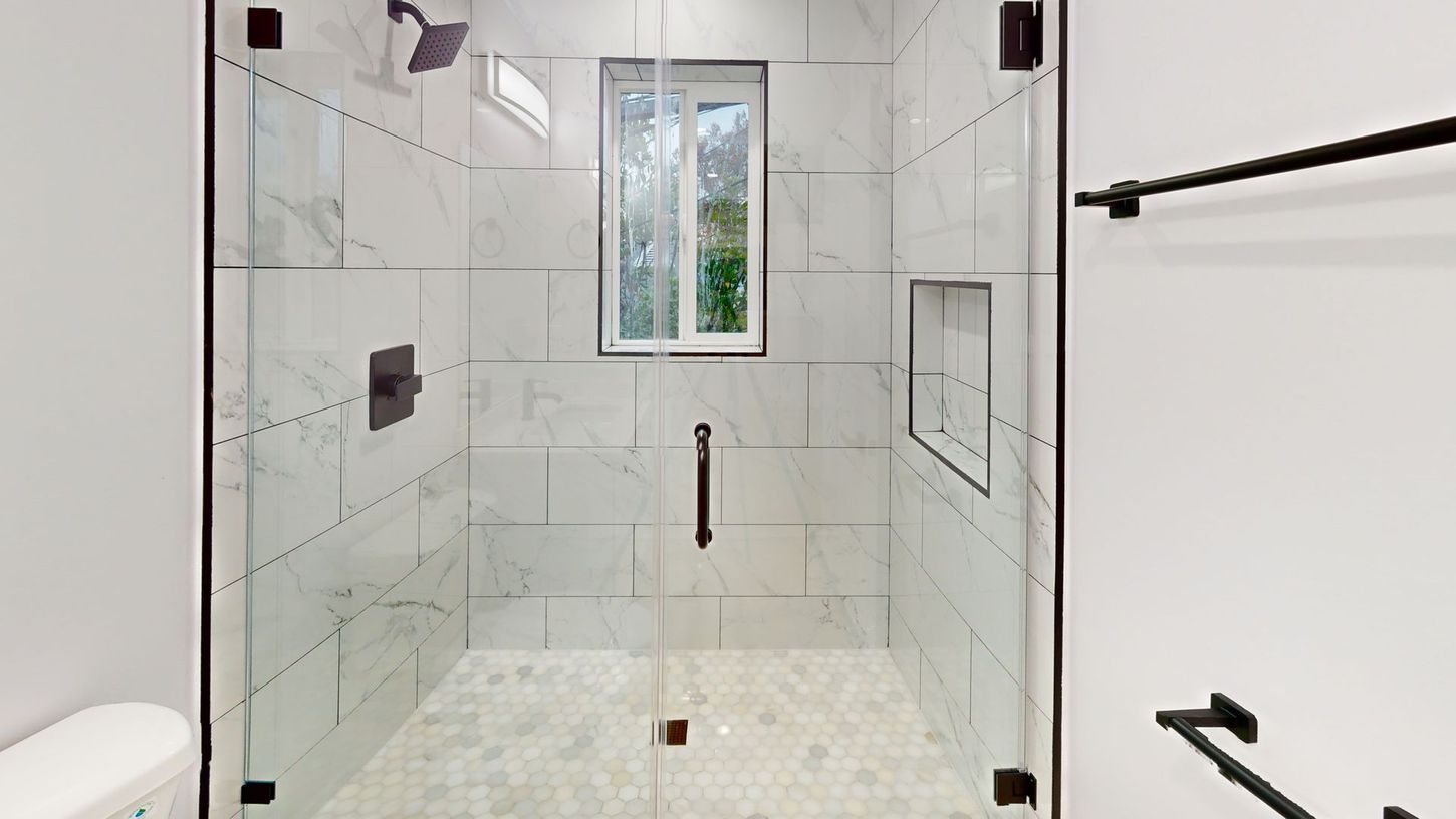 Glass shower with white marble tile, black fixtures, and a small window.