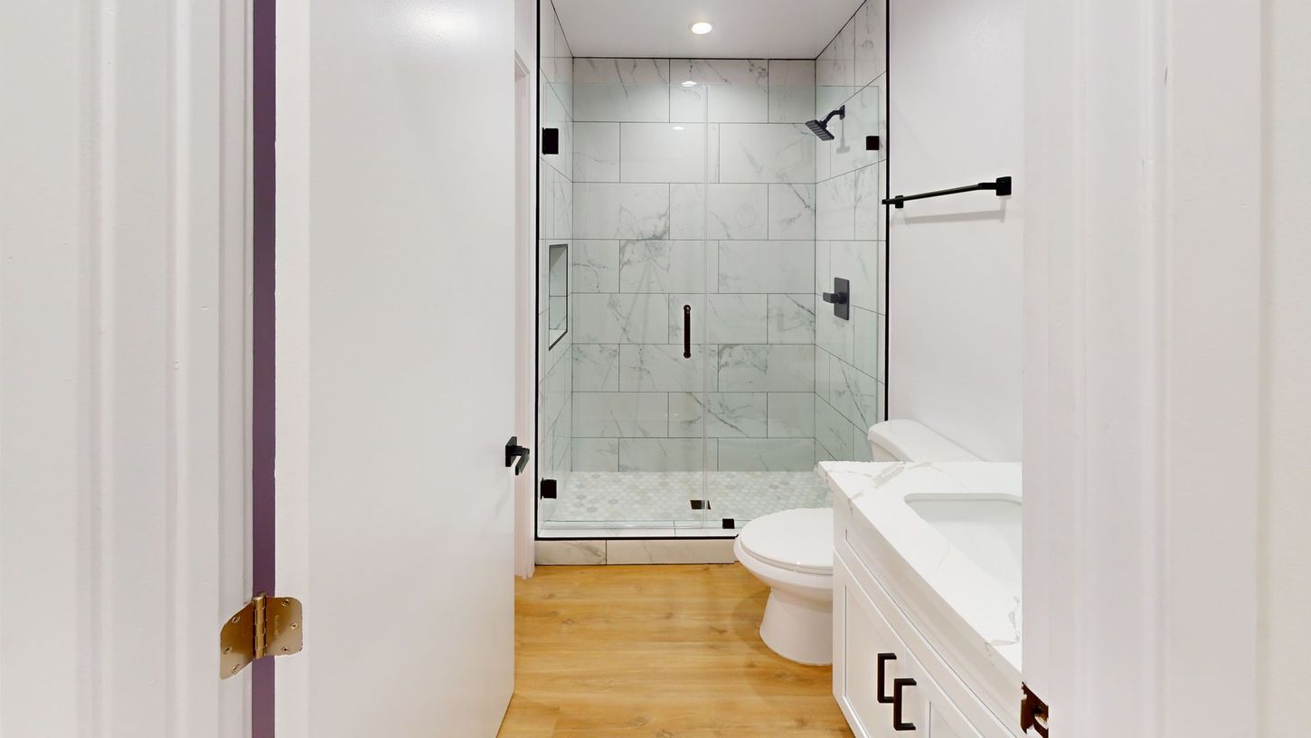 Bathroom with marble shower, white vanity, black fixtures, and wood-look flooring.