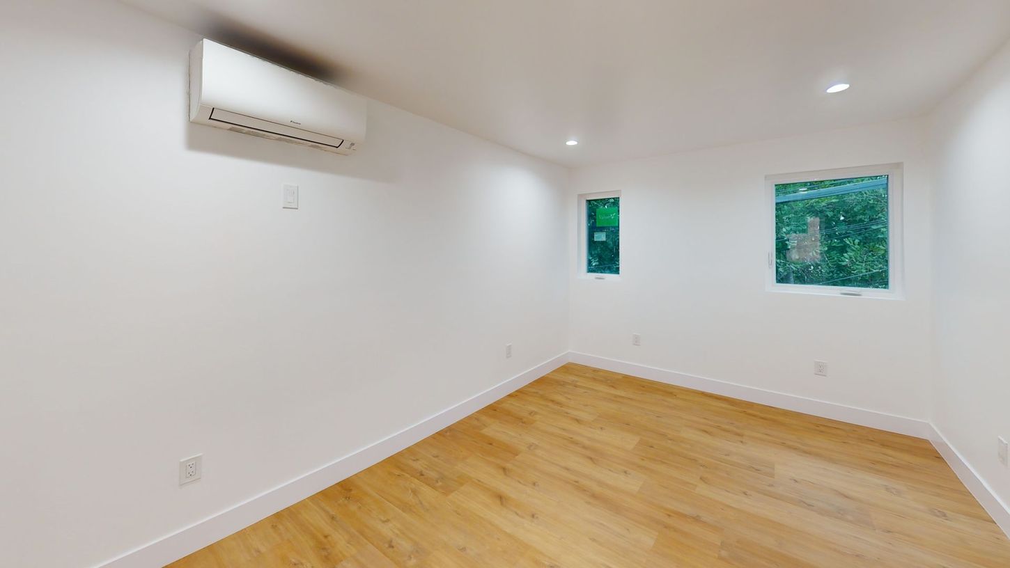 Empty room with wood floor, white walls, two windows, and an air conditioner.