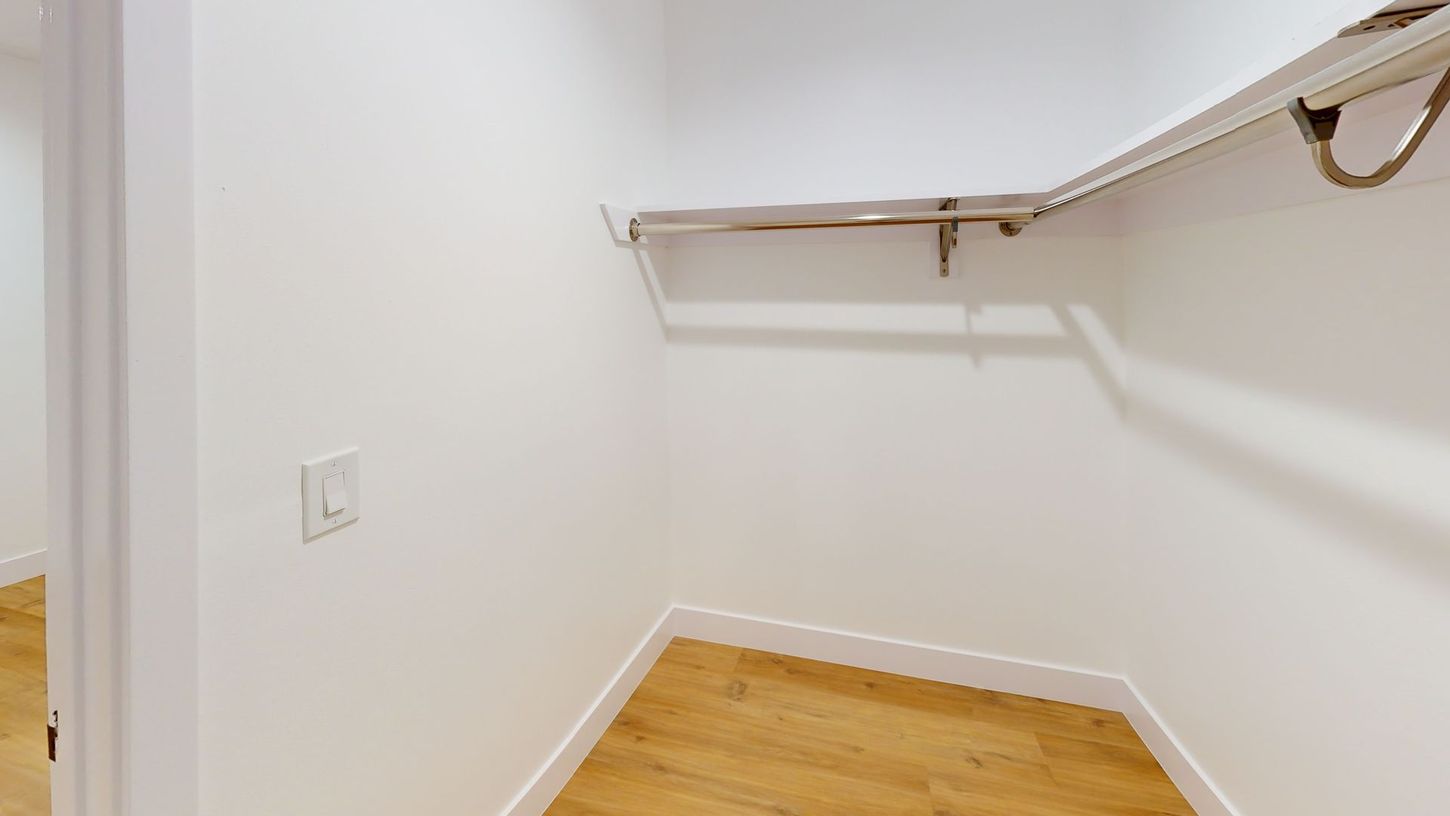 Empty white walk-in closet with wooden floor and a shelf.